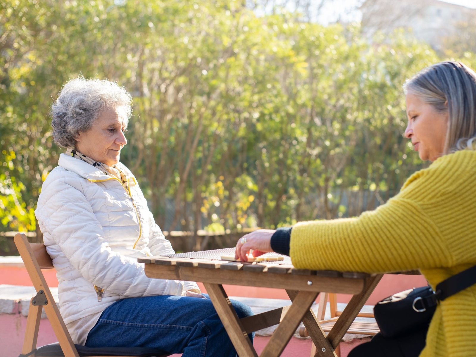 Caregiver and an older woman playing dominoes at a backyard table