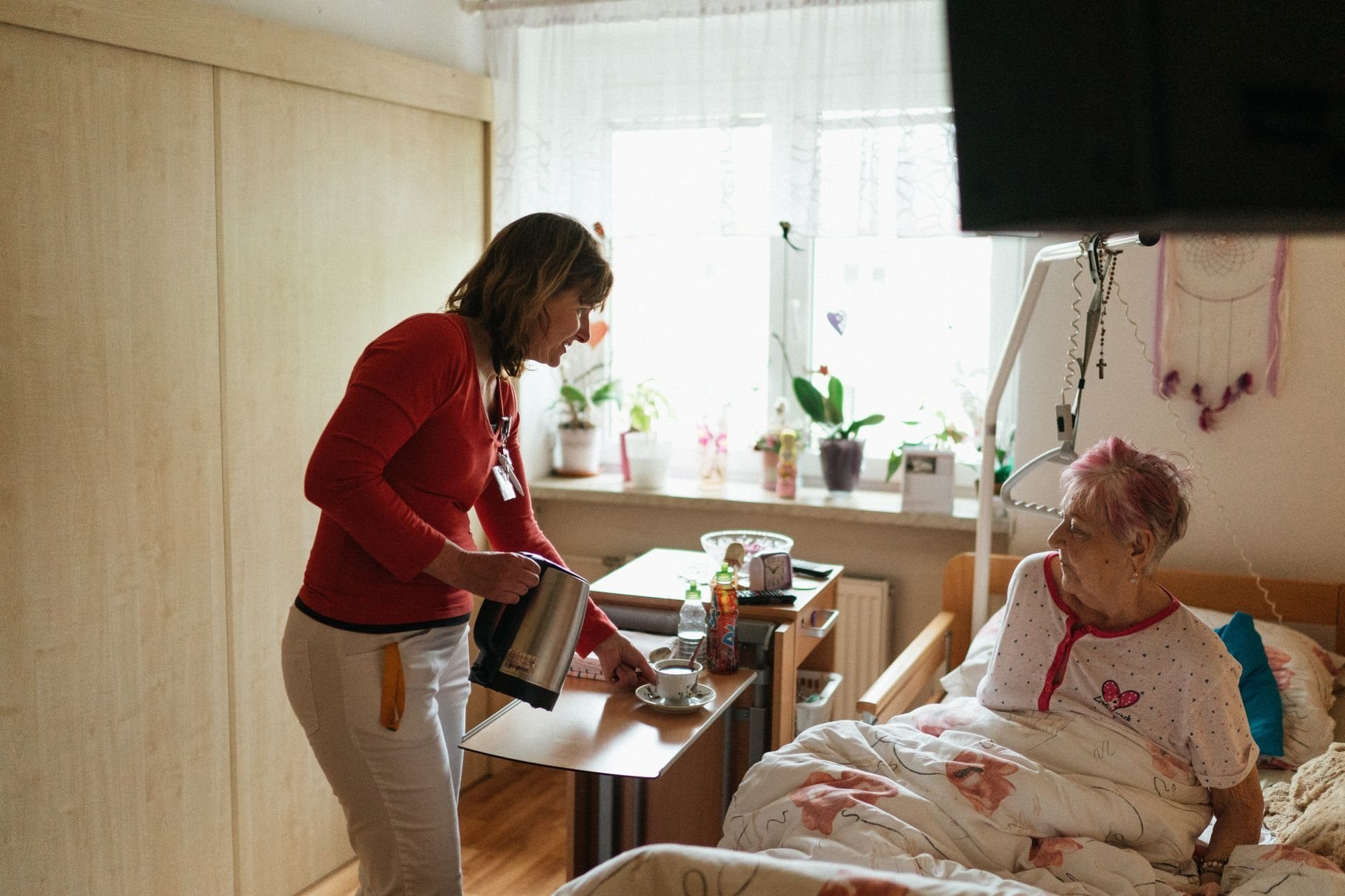 Caregiver bringing a warm drink to a woman resting in bed