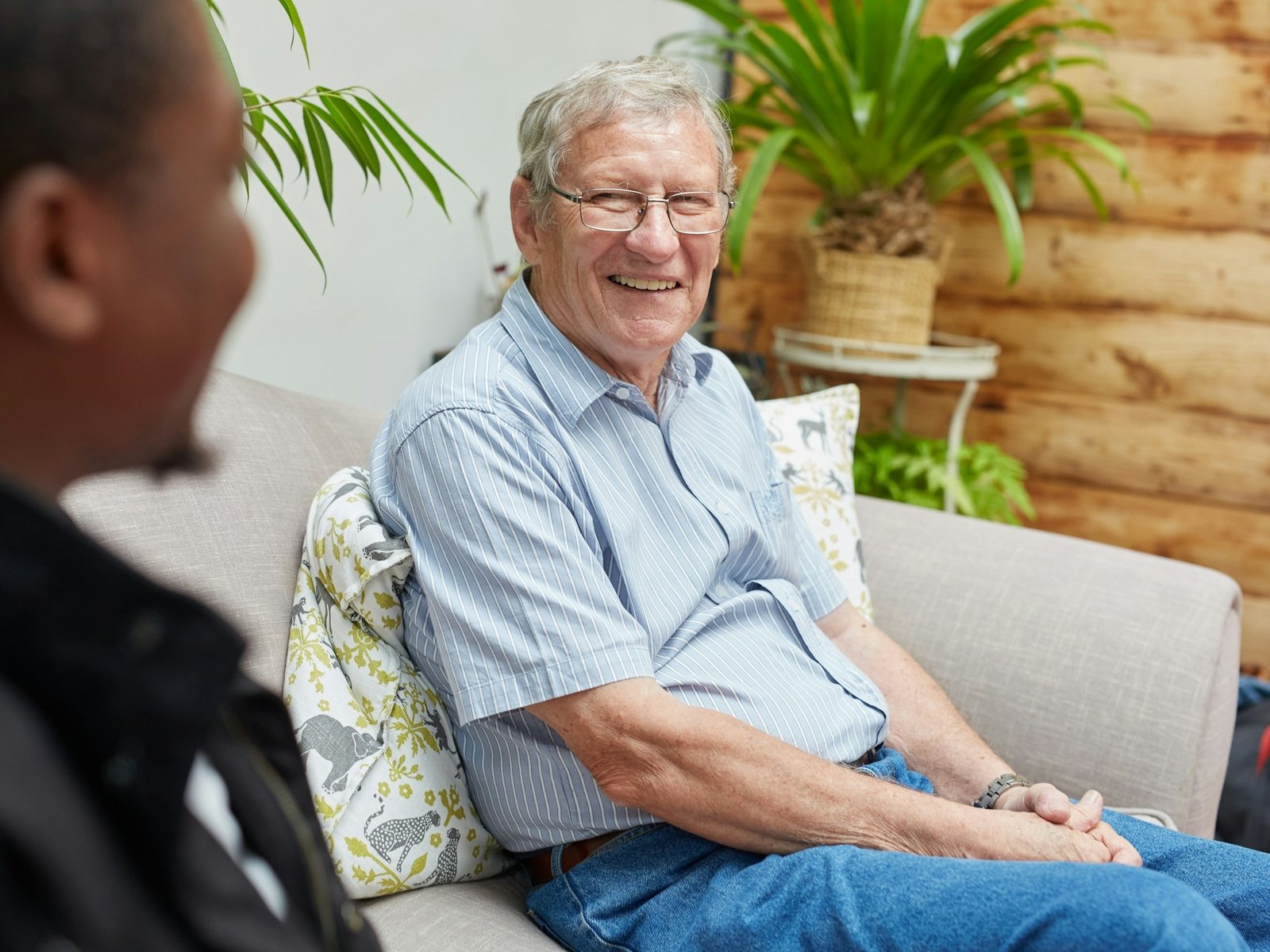 An older man laughing on his sofa during a visit from his caregiver