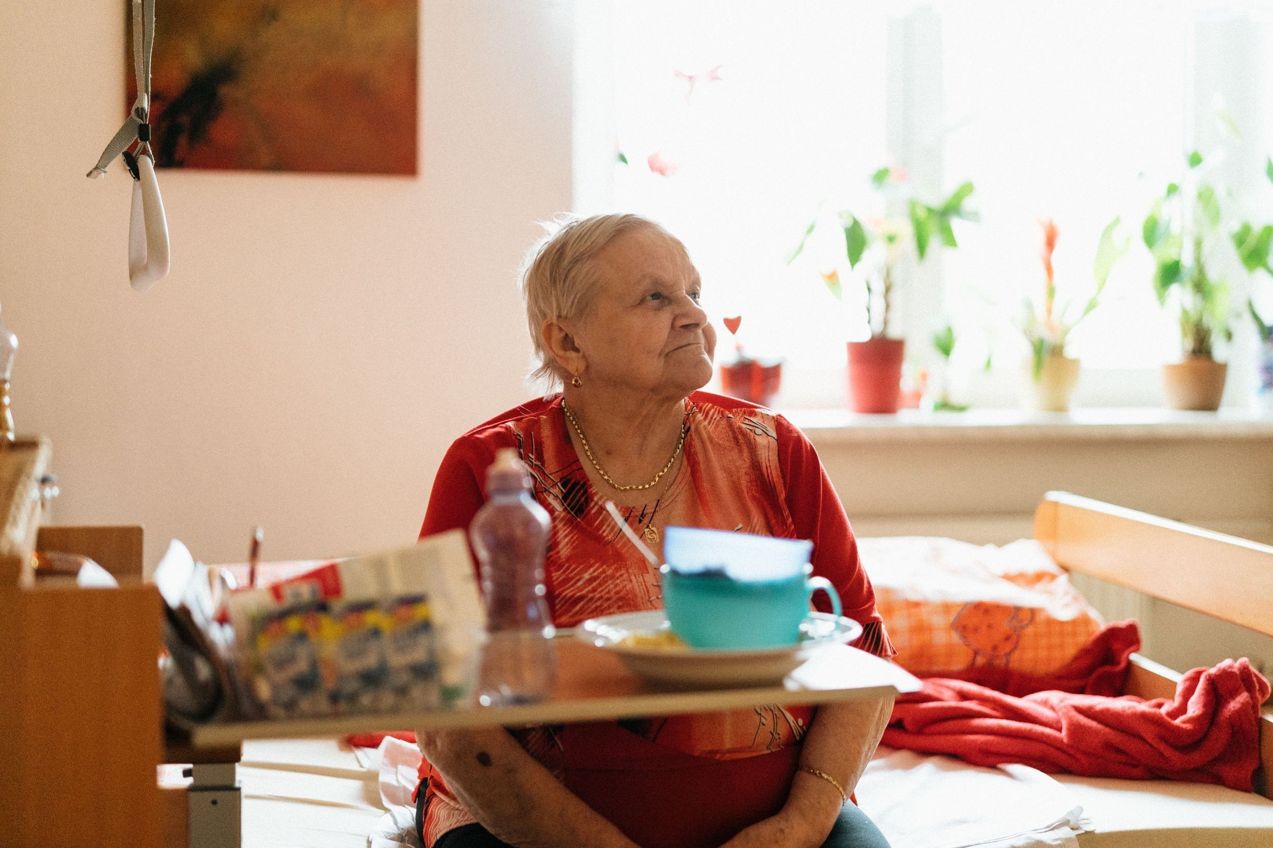 An older woman sitting up by a sunny window with her lunch tray